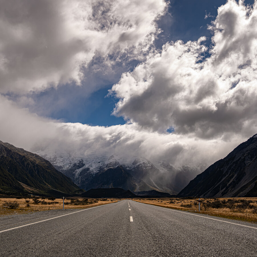 An empty road leading into a cloud-covered mountain valley