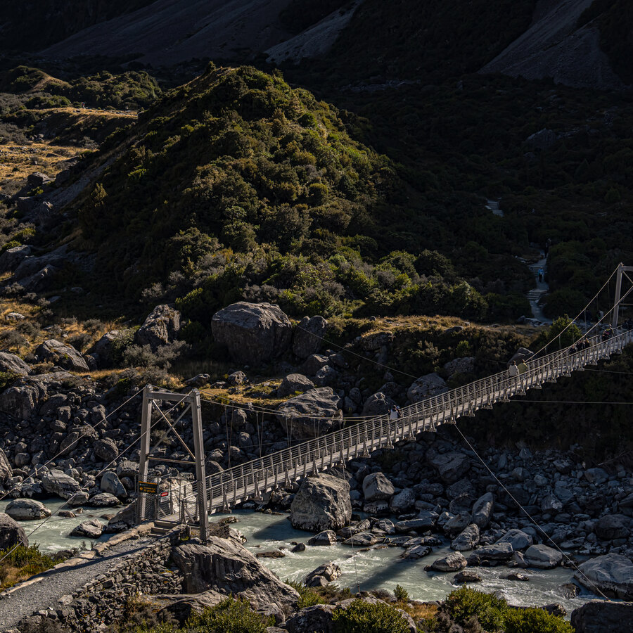 A narrow suspension bridge crossing a rocky alpine stream