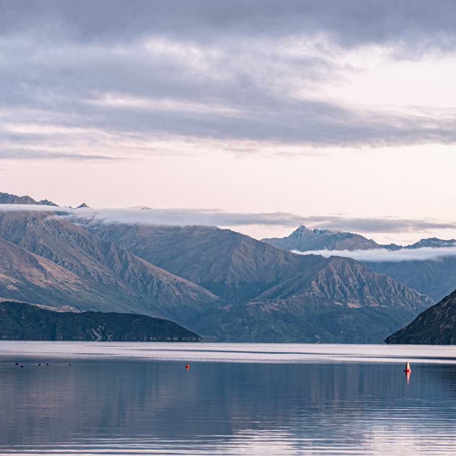 A quiet lake and layered ridges under a pale evening sky