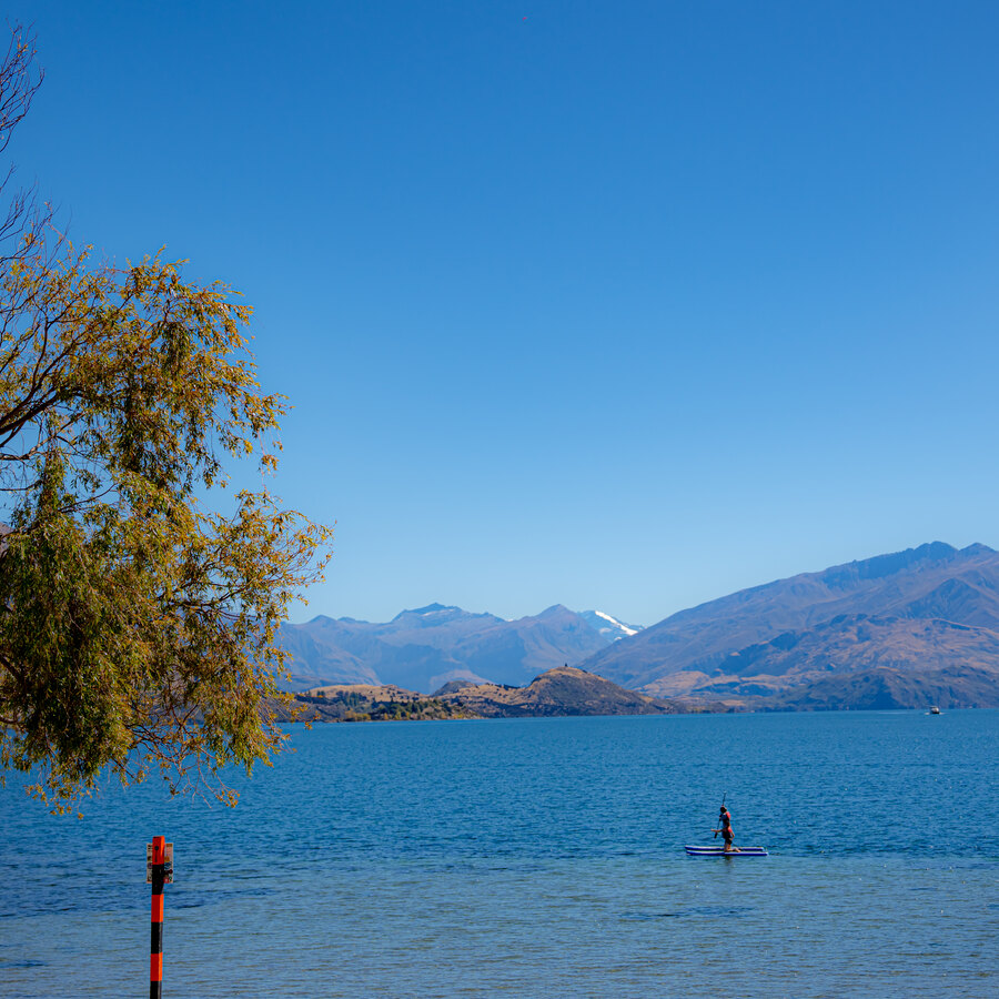 A vivid blue lake with a distant paddleboarder and mountain ridge