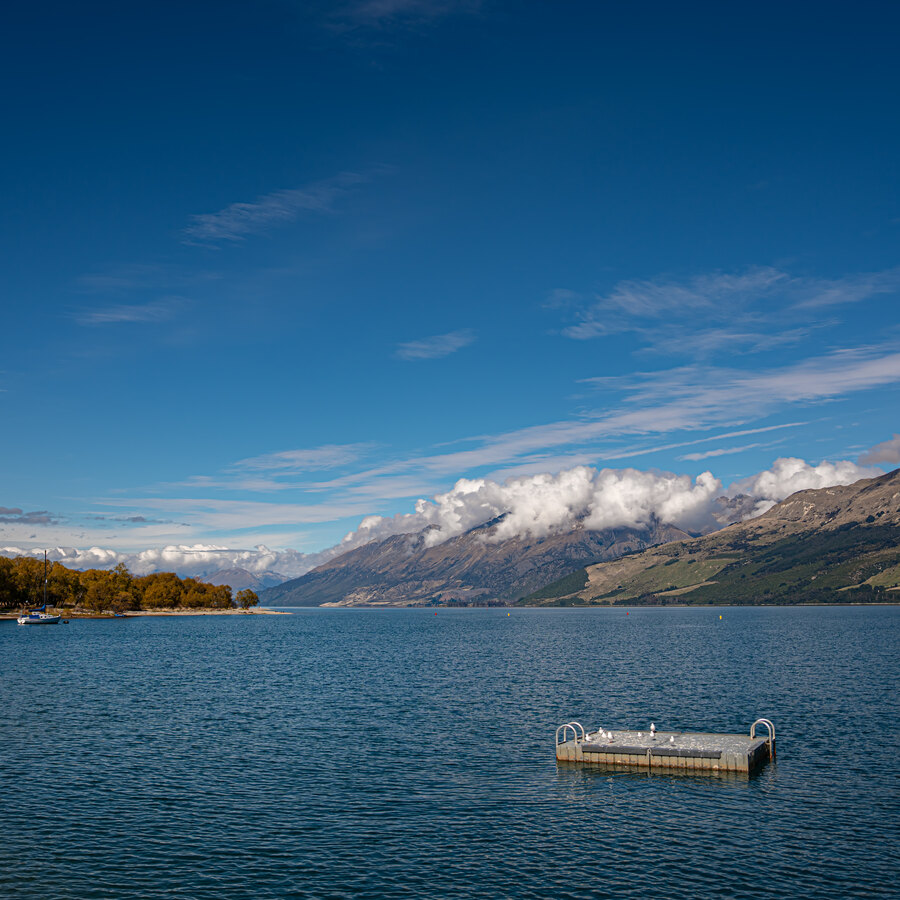 A small floating platform on a blue lake beneath a long mountain ridge