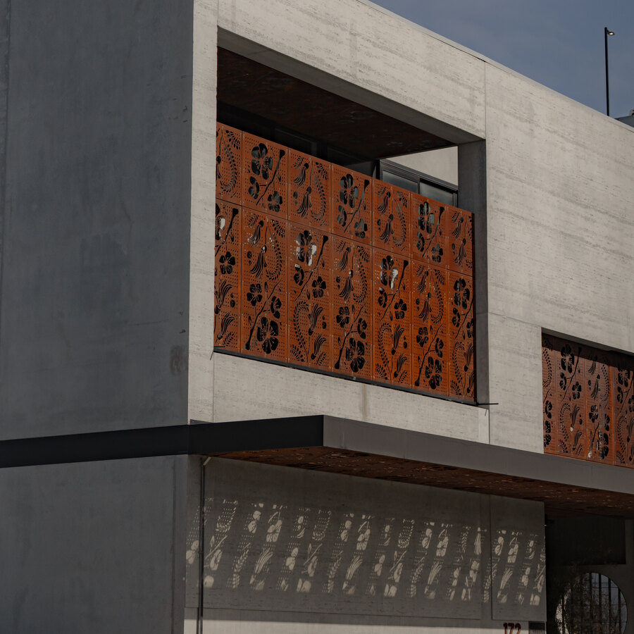 A concrete facade with weathering-steel screens and patterned shadows